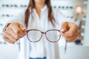 An optometrist examines an adult patient's eyes with specialized equipment in a clinical setting.