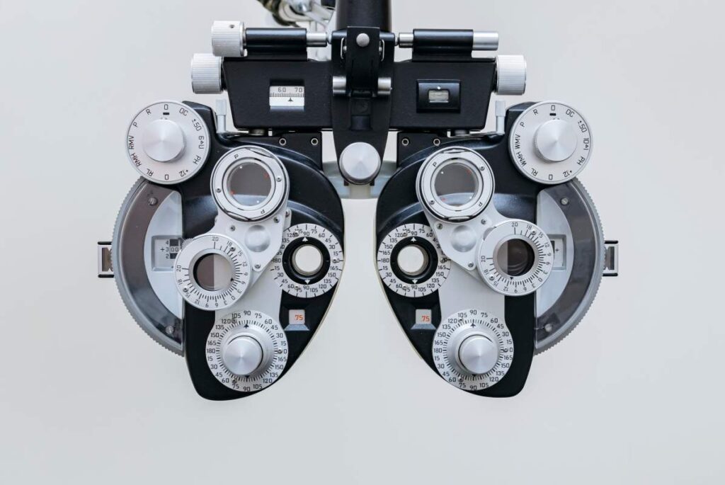 A woman sitting near a window rubbing her eyes, with a small humidifier and digital devices on the table.