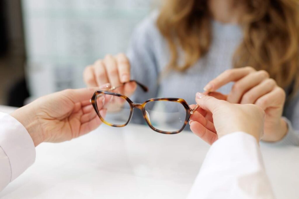 A close-up of a person studying a paper eyeglasses prescription at a kitchen table.